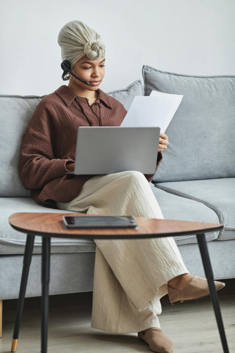Woman with headset reviewing documents while working from home on a laptop.